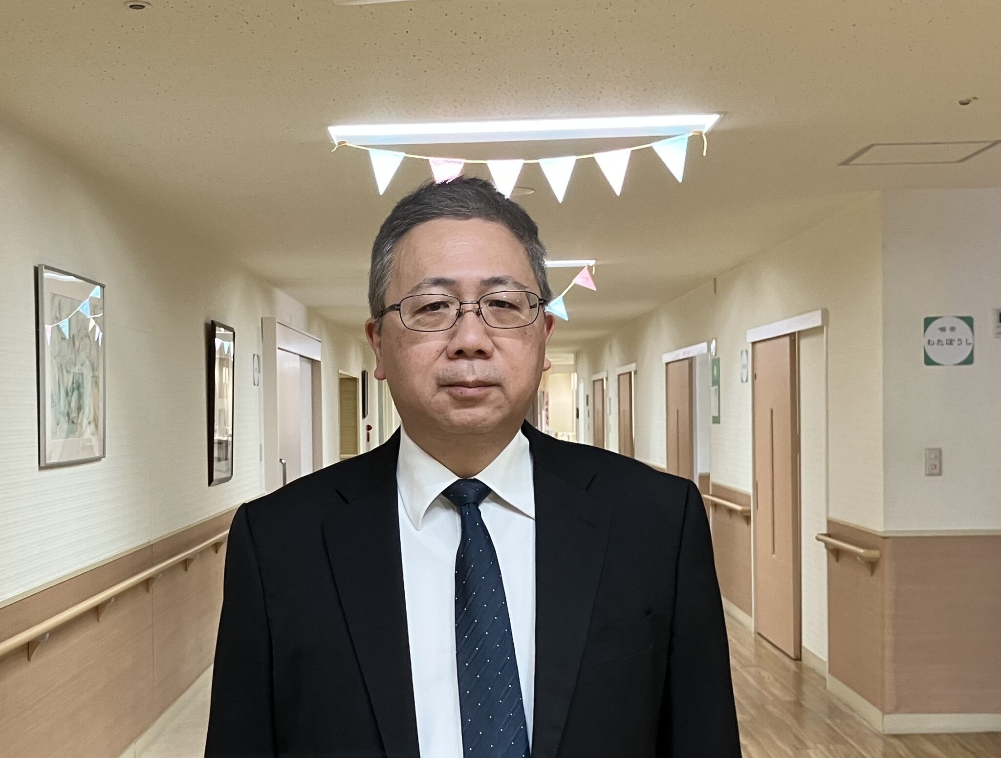 介護施設の廊下でスタッフが撮影された写真。施設内部の実空間が背景に映っている。